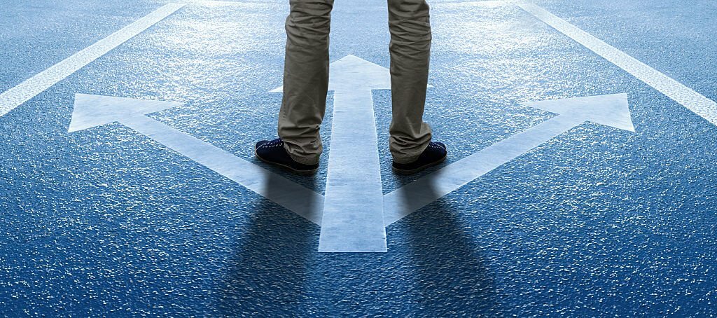 Man standing on arrows painted on the asphalt. Bright light in the background.