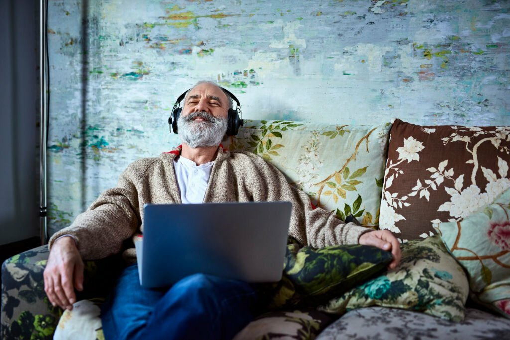 Man in his 50s relaxing at home, with laptop and eyes closed, enjoying music, escapism, satisfaction, happiness